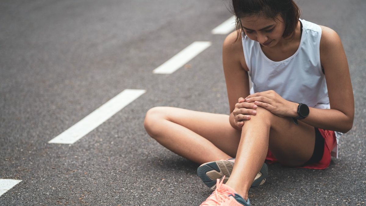 Woman runner sits on ground and holds knee