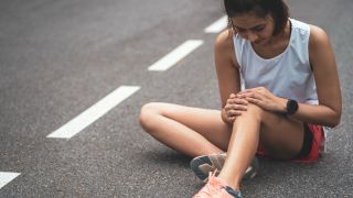 Woman runner sits on ground and holds knee
