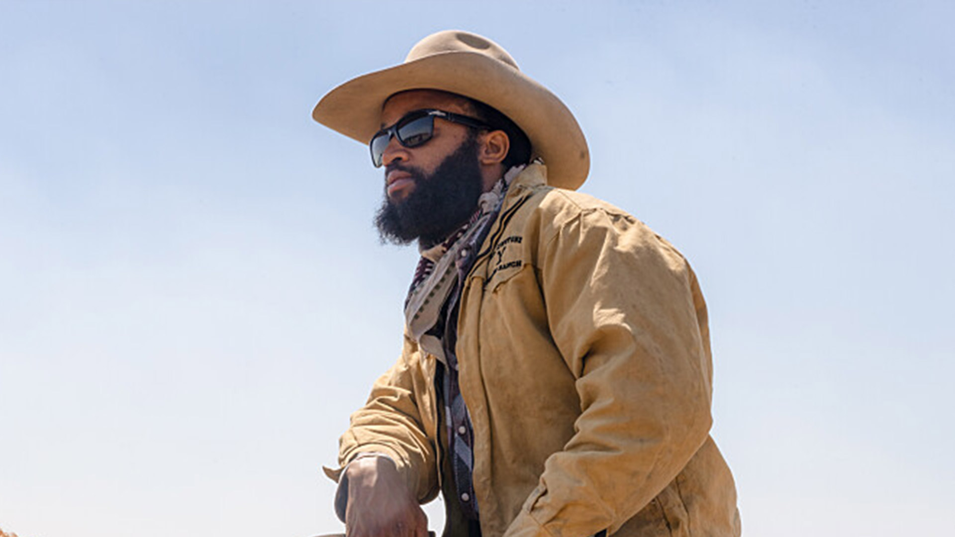 A man sits on a horse in cowboy attire with glasses on