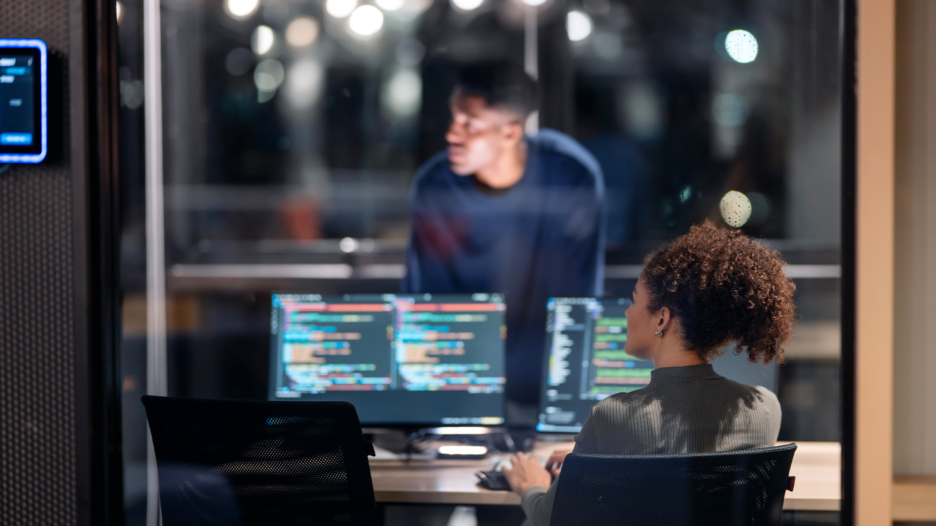 Male and female cybersecurity specialists collaborating in an open plan office space, looking at screen during cyber attack recovery program.