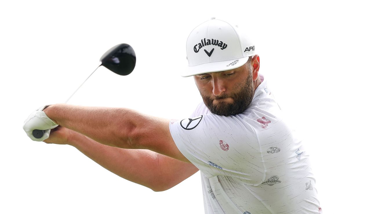 Jon Rahm hits a drive whilst wearing a white Callaway hat