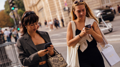 two women wearing sunglasses on their heads looking at their phones while walking on the street 