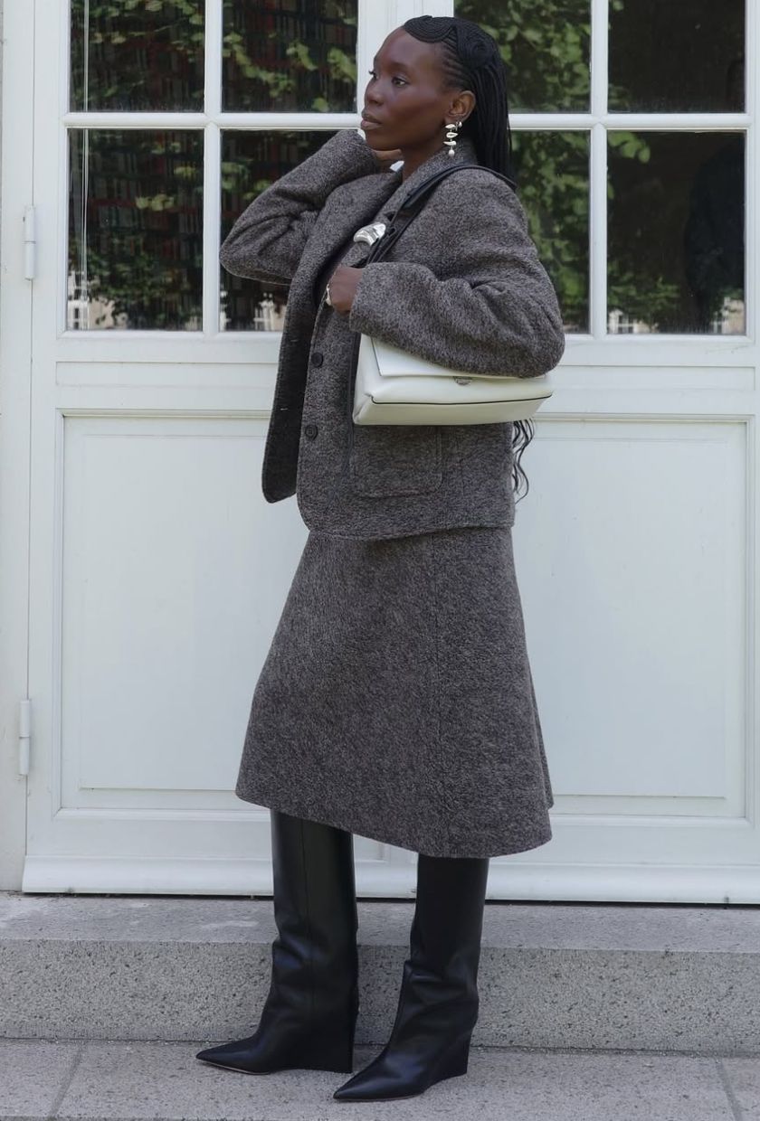 @daniellejinadu wears a grey chunky cardigan, wool skirt, black knee-high boots and white shoulder bag