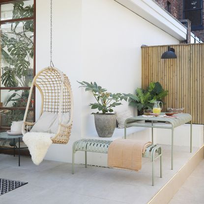 A patio with a sage green HAY Palissade metal outdoor dining set with ahanging rattan egg chair next to it