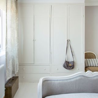 White bedroom with white double wardrobe, white wooden floor, and a bag hanging from wardrobe handle