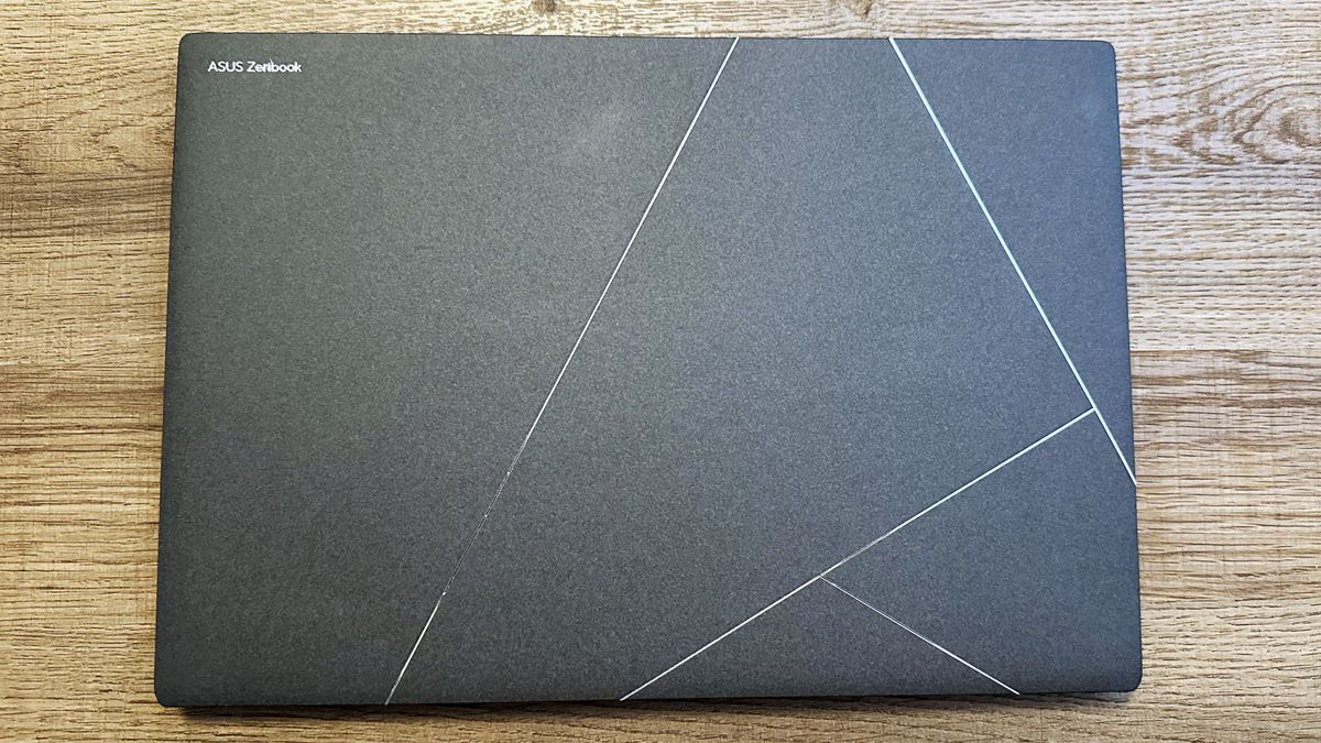 Asus Zenbook S 14 closed on a wooden table showing the lid with stylized Asus logo.