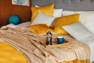 Yellow and white bedding with a cafetiere. cup of tea and a c