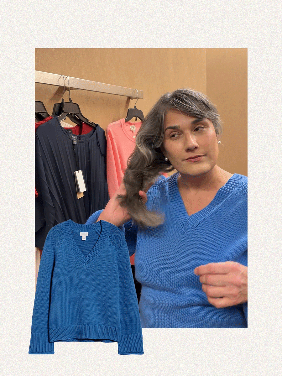 A woman with gray hair trying on a blue v-neck sweater.