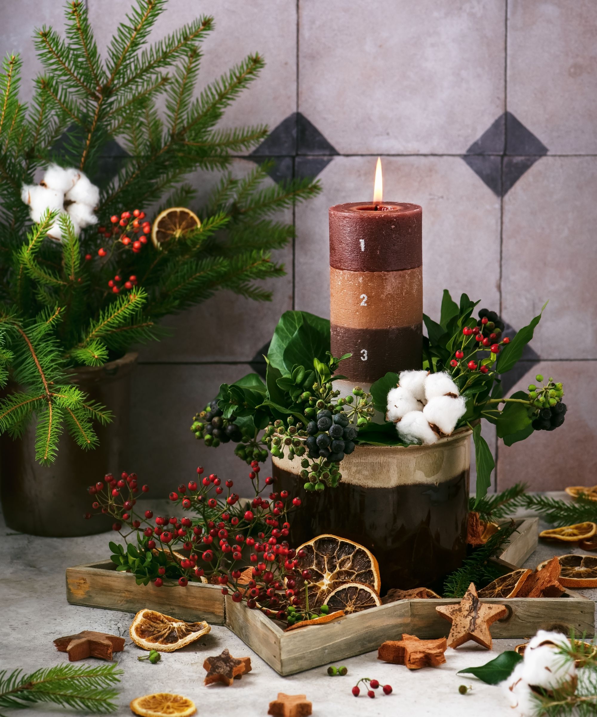 Burning Christmas layers candle with 4 Advent numbers decorated with natural material, slices of dried orange, fir, ivy and rose hip berries branches