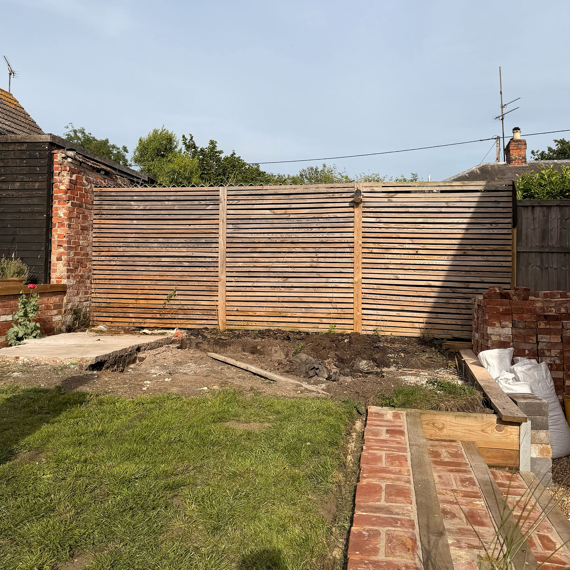 Garden mid-renovation, with dug-up lawn area beside wooden fence
