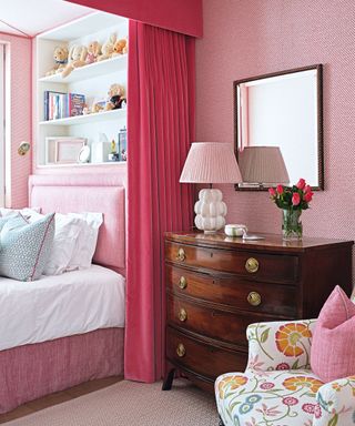 pink bedroom with wooden chest of drawers and open shelving above bed