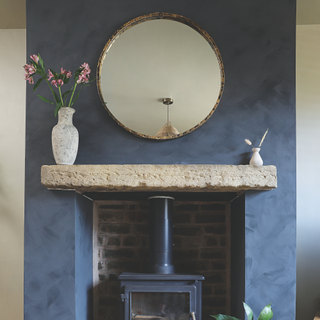 Rustic fireplace with blue walls. There is a circle mirror and two small vases on the mantle