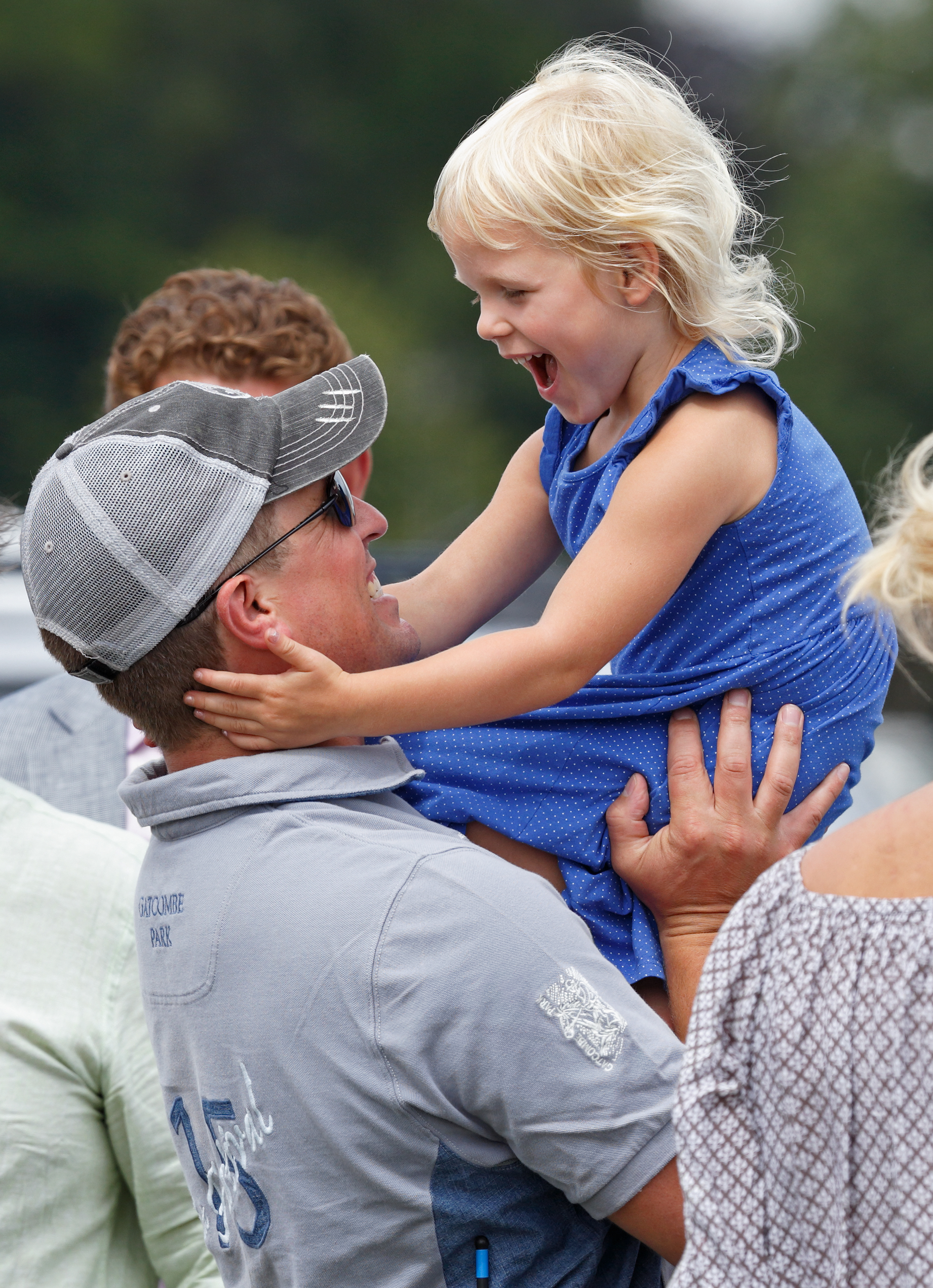 Peter Phillips wearing a gray baseball hat holding his daughter Isla and laughing