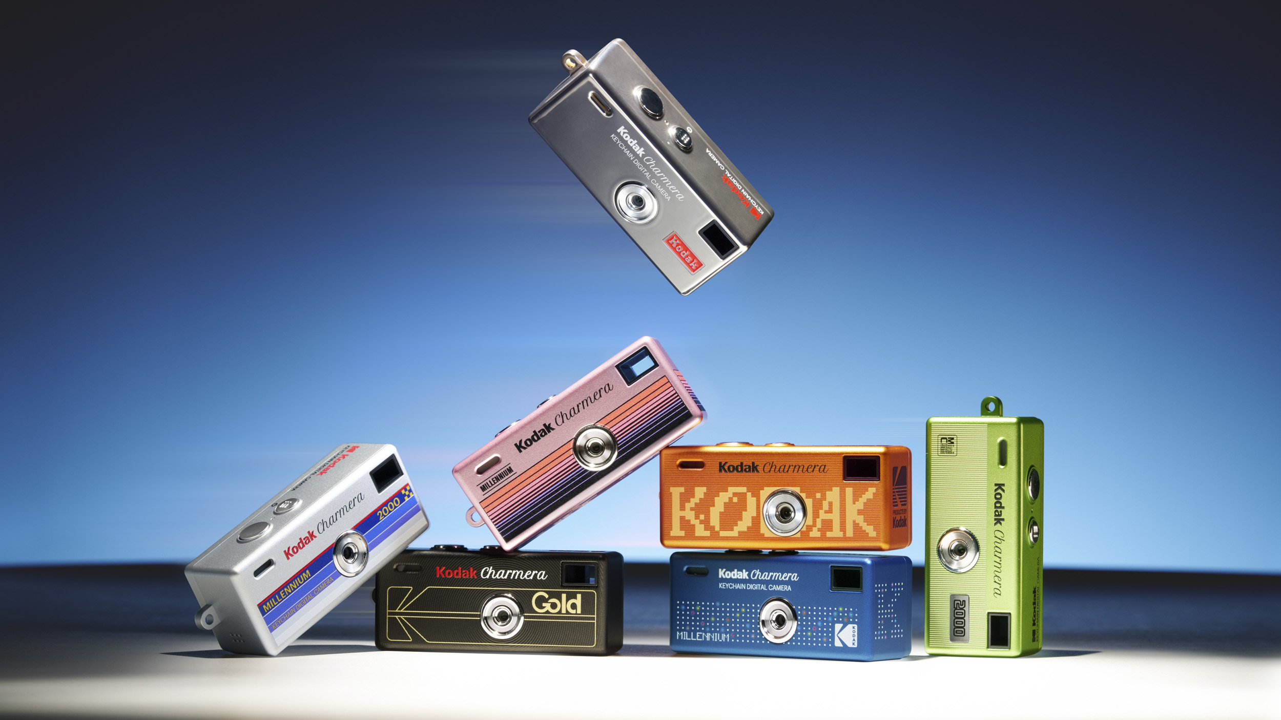 Seven different Kodak Charmera Millennium Edition cameras in a studio on a white surface with bright blue backdrop