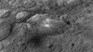 black and white image of a crater on the dwarf planet ceres with bright white material on its floor