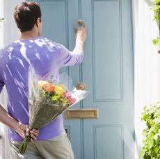 man at door with flowers behind his back