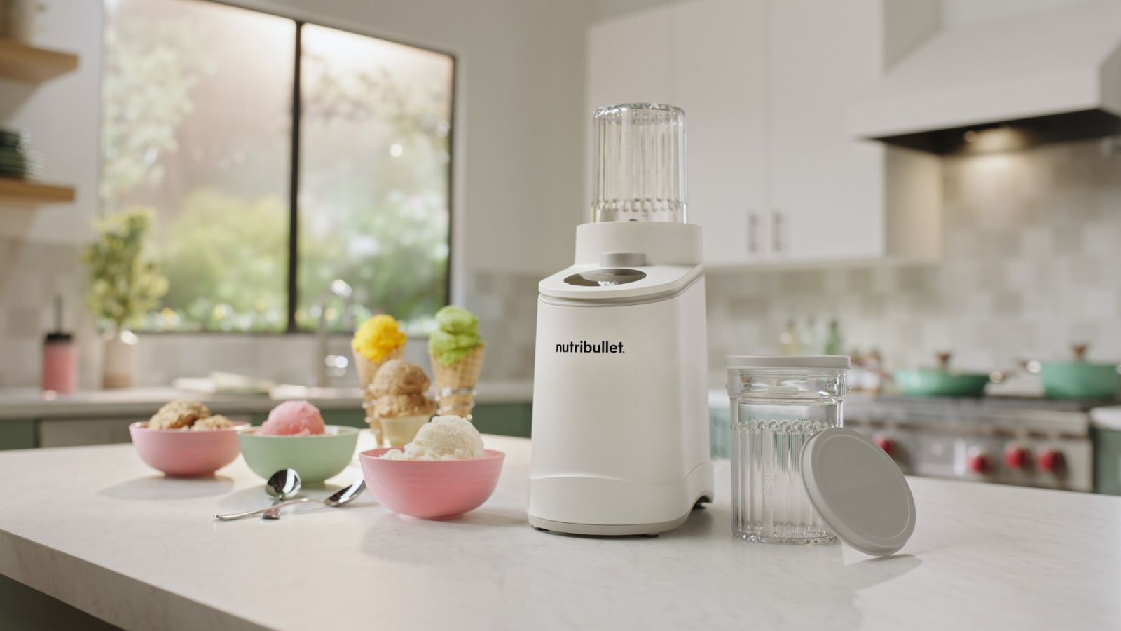A white Nutribullet Chill ice cream maker on a white kitchen counter surrounded by small bowls of ice cream. 