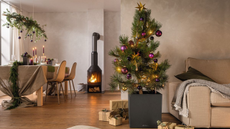 A potted Christmas tree next to a sofa with a throw on top. There is also a view of the dining table with foliage on top and a hanging green ornament above the table.