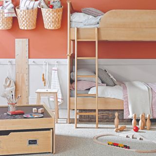 A coral-painted children's bedroom with a bunk bed, storage baskets hanging on the wall and toys scattered across the floor
