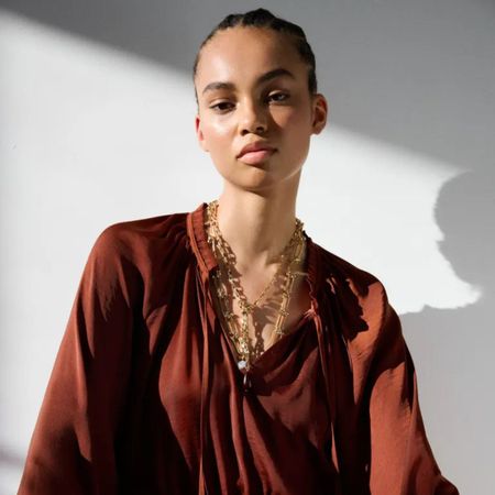 Woman wears burnt orange blouse, layered gold necklaces