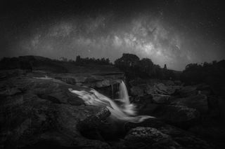 A black and white landscape with a waterfall at night