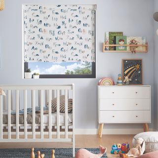 White nursery with white cot and chest of drawers and patterned roller blind