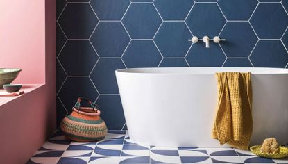 An example of how to design a bathroom showing a white bath in front of large blue hexagonal wall tiles next to a pink wall