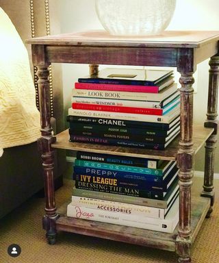 A rustic and ornate three tiered nightstand with neatly stacked books and a bulbous round glass decor item on top