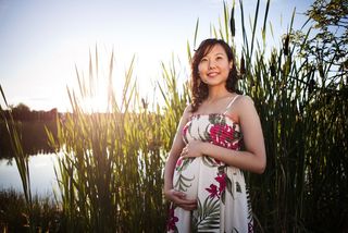A pregnant woman poses by a pond.