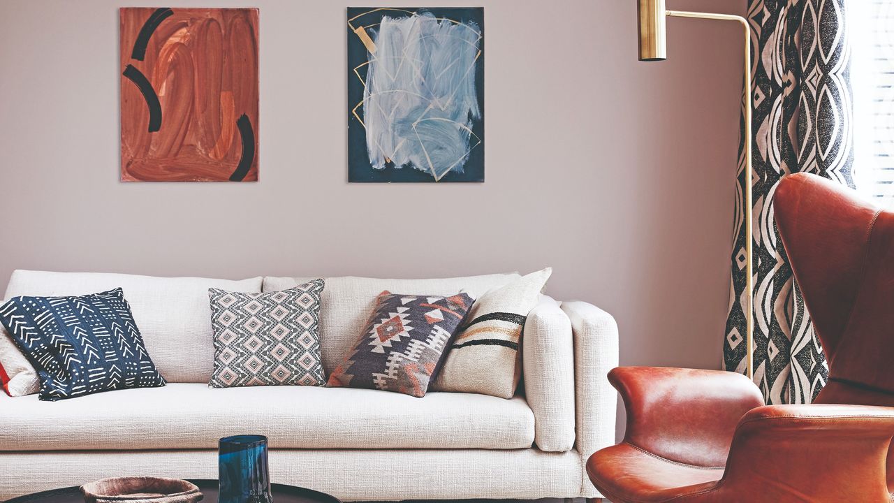 A pink-painted living room with a cream sofa, a brass floor lamp and two hanging artworks