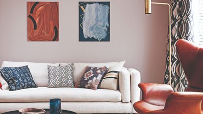 A pink-painted living room with a cream sofa, a brass floor lamp and two hanging artworks