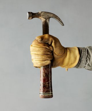 A workman holding a wooden handled hammer with DIY gloves on