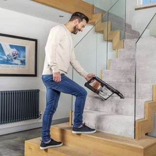 A man using a Shark IZ300UK vacuum cleaner to clean carpeted stairs