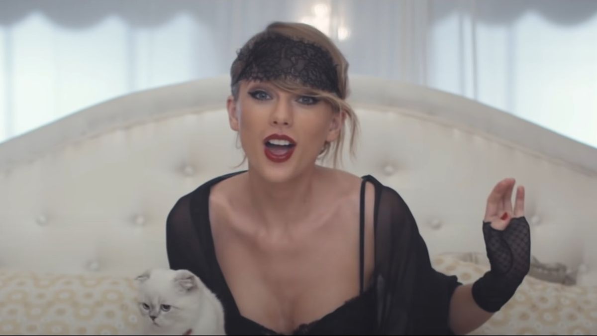 Taylor Swift in a night gown with a black eye mask on top of her head. She&#039;s holding her cat while singing Blank Space.