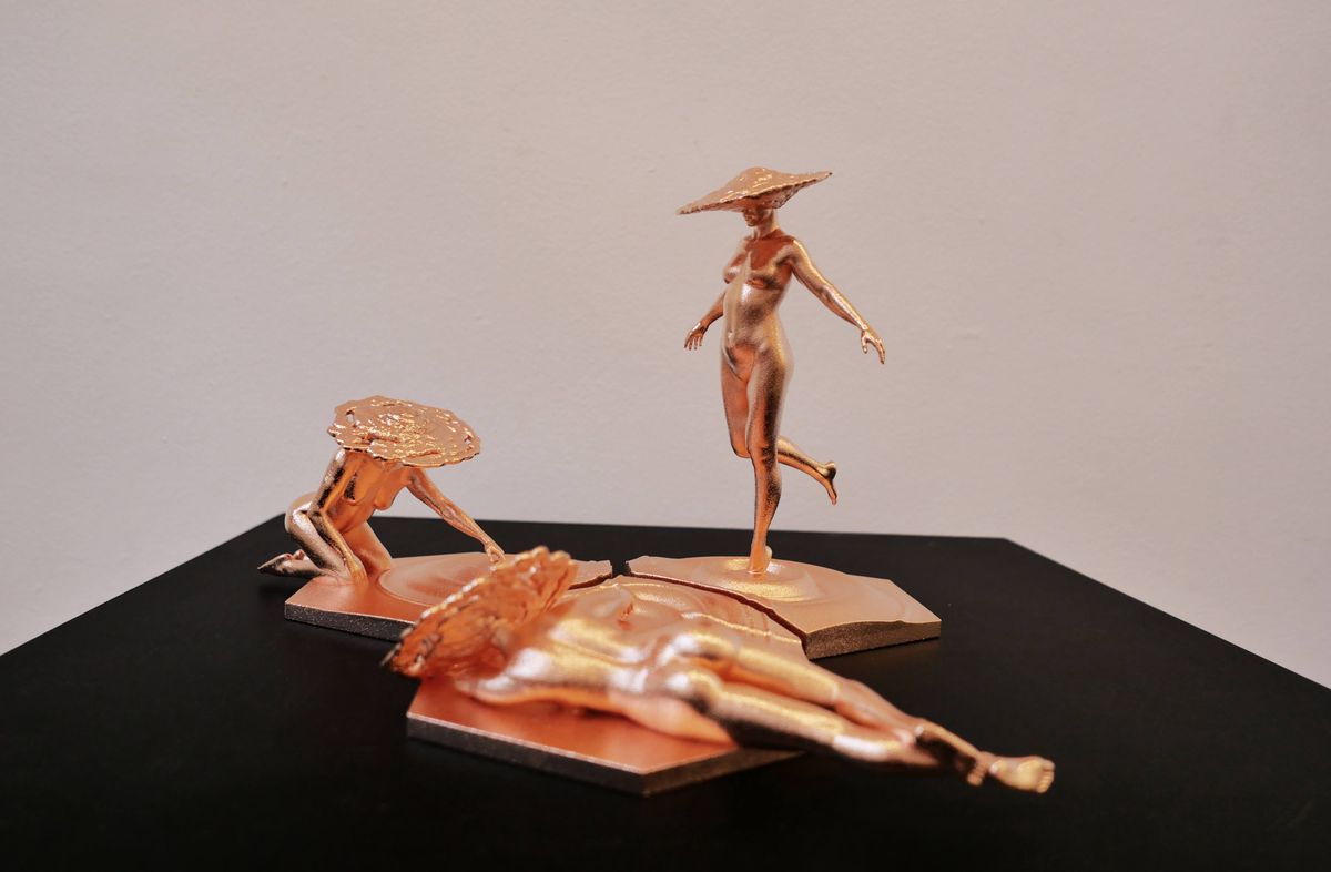 Two golden figures with large hats interact in a small metal sculpture on top of a dark surface.