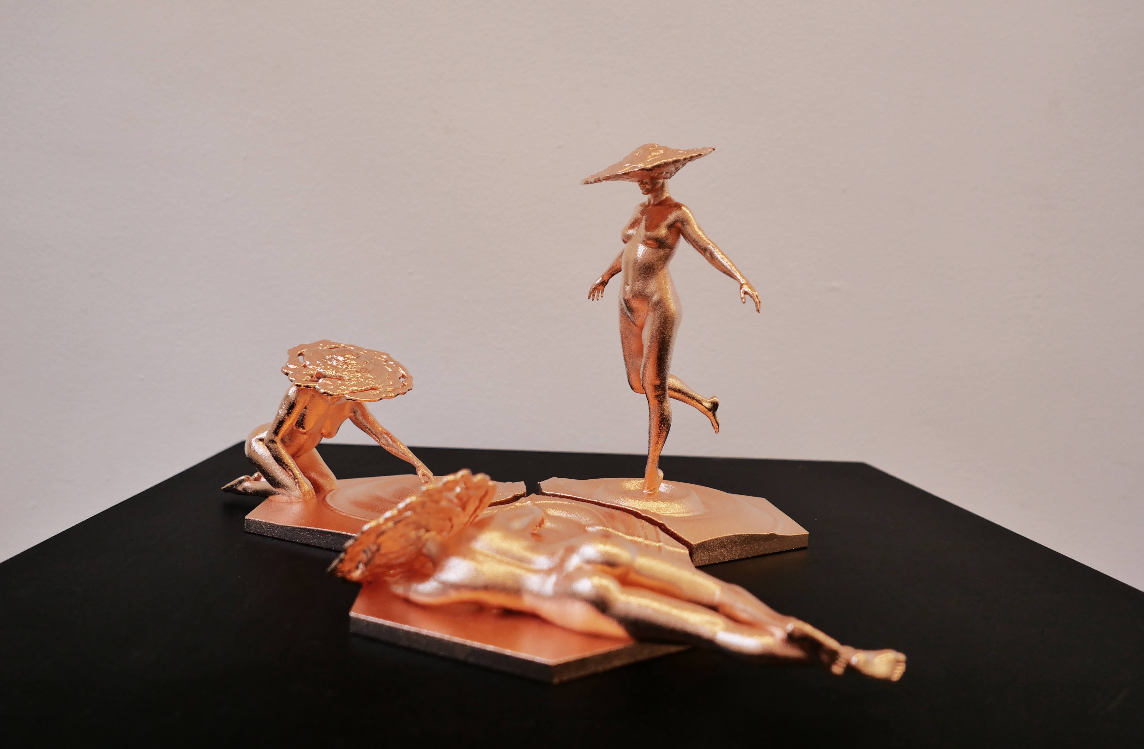 Two golden figures with large hats interact in a small metal sculpture on top of a dark surface. 