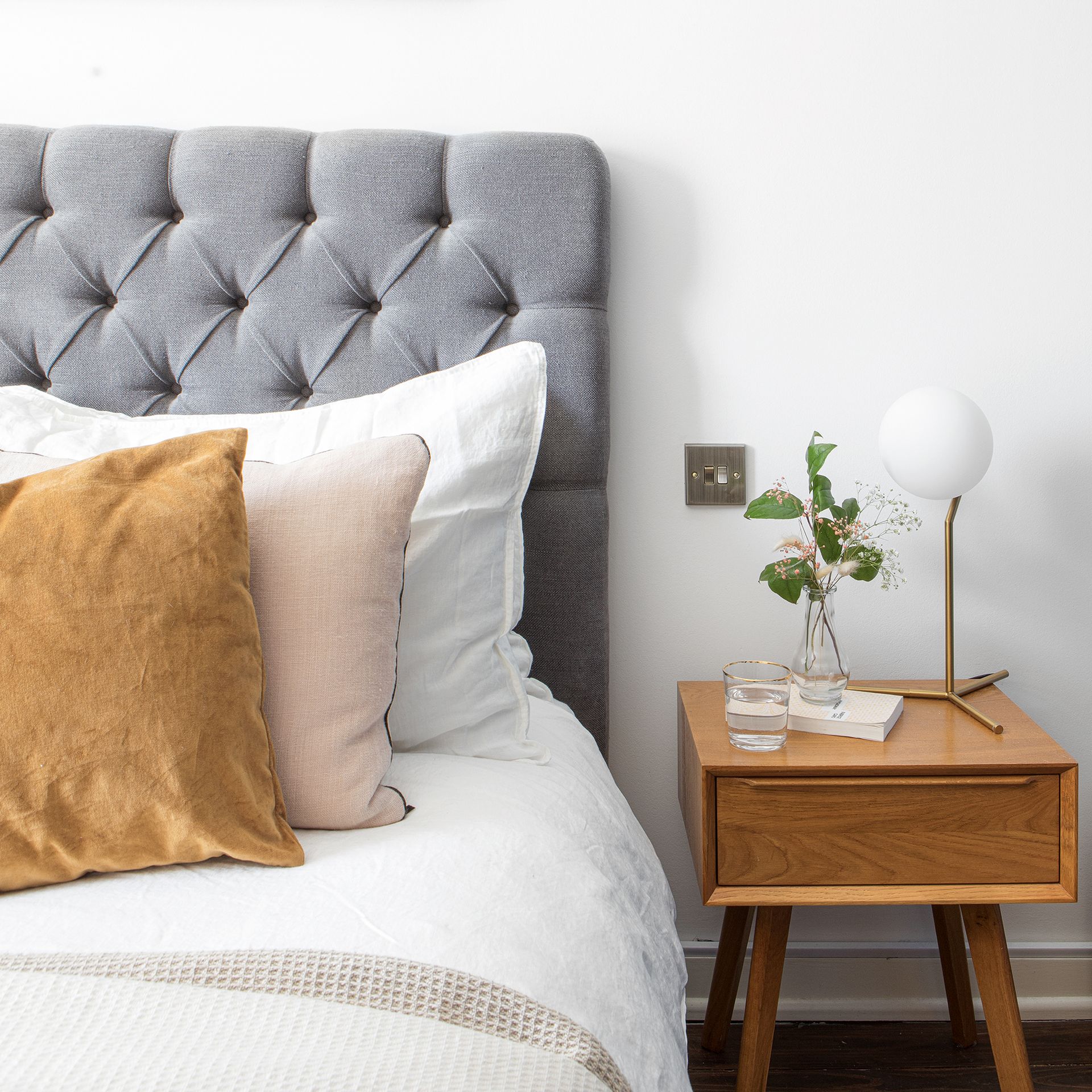 Bed with grey upholstered headboard and wooden bedside table