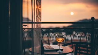A glass of rose wine on the balcony of a hotel, next to a laptop