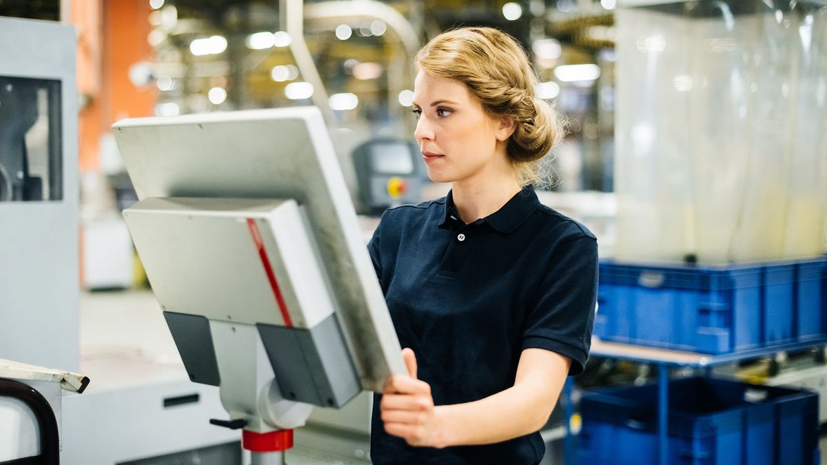 A woman looking at a computer terminal attached to a machine in a factory.