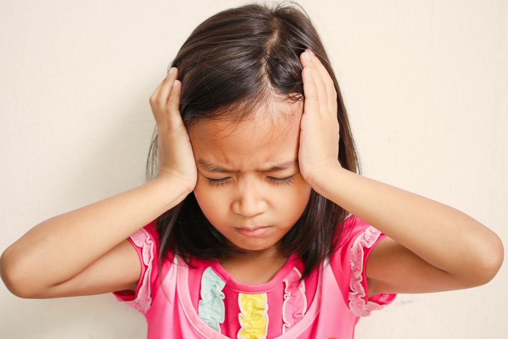 A little girl holds her head in pain