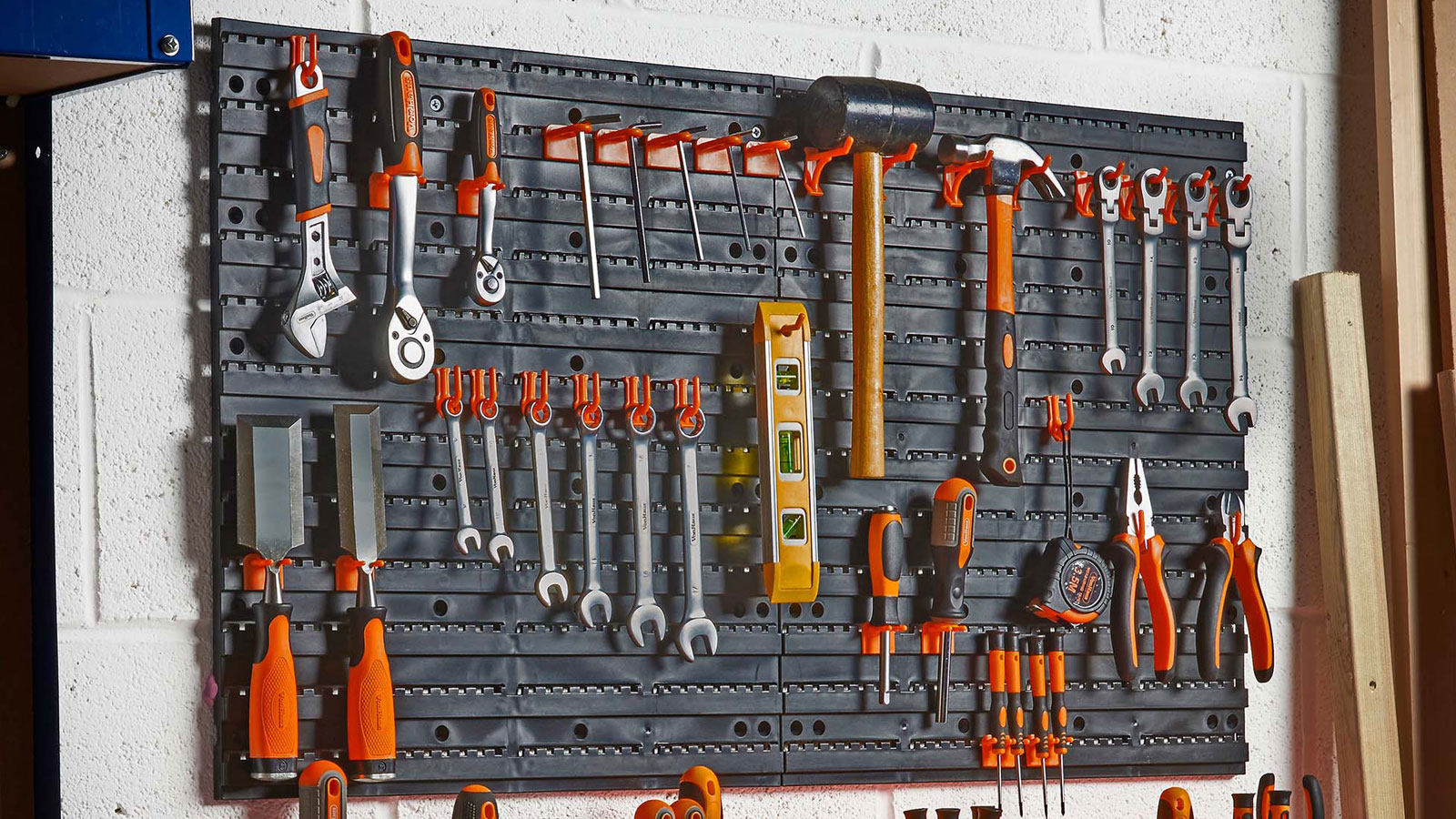 Wall-mounted pegboard with various orange hand tools on a white block wall