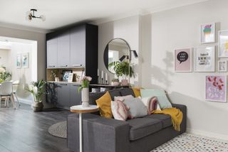 Family room with grey sofa, white side table, and black ceiling-to-floor storage unit next to open shelving