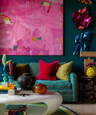 maximalist living room corner with teal sofa, dark teal walls, red and green cushions and bright pink abstract artwork canvas