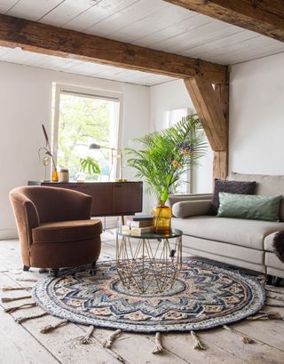 a living room space with natural lighting, white walls, a seating area or sofa and armchair and tasseled rug