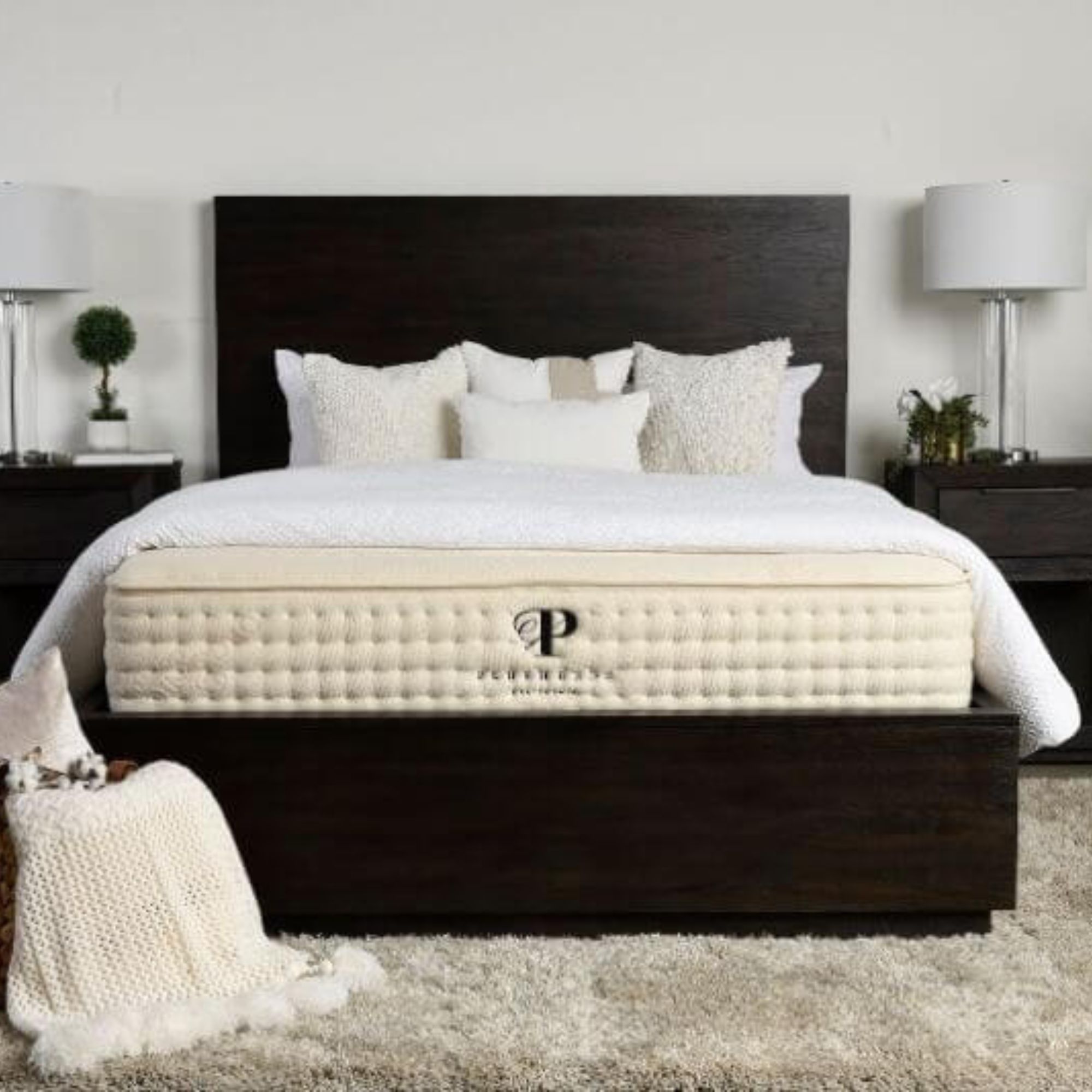 A Plushbeds mattress on a bed with pillows against a white wall.