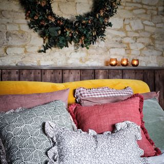 Bed with layers of coloured and patterned pillows and natural wreath on wall