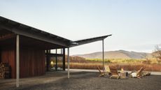 An image of an angular roof with the Catskill mountains in the distance, plus a fire pit with wooden lounge chairs in the foreground.