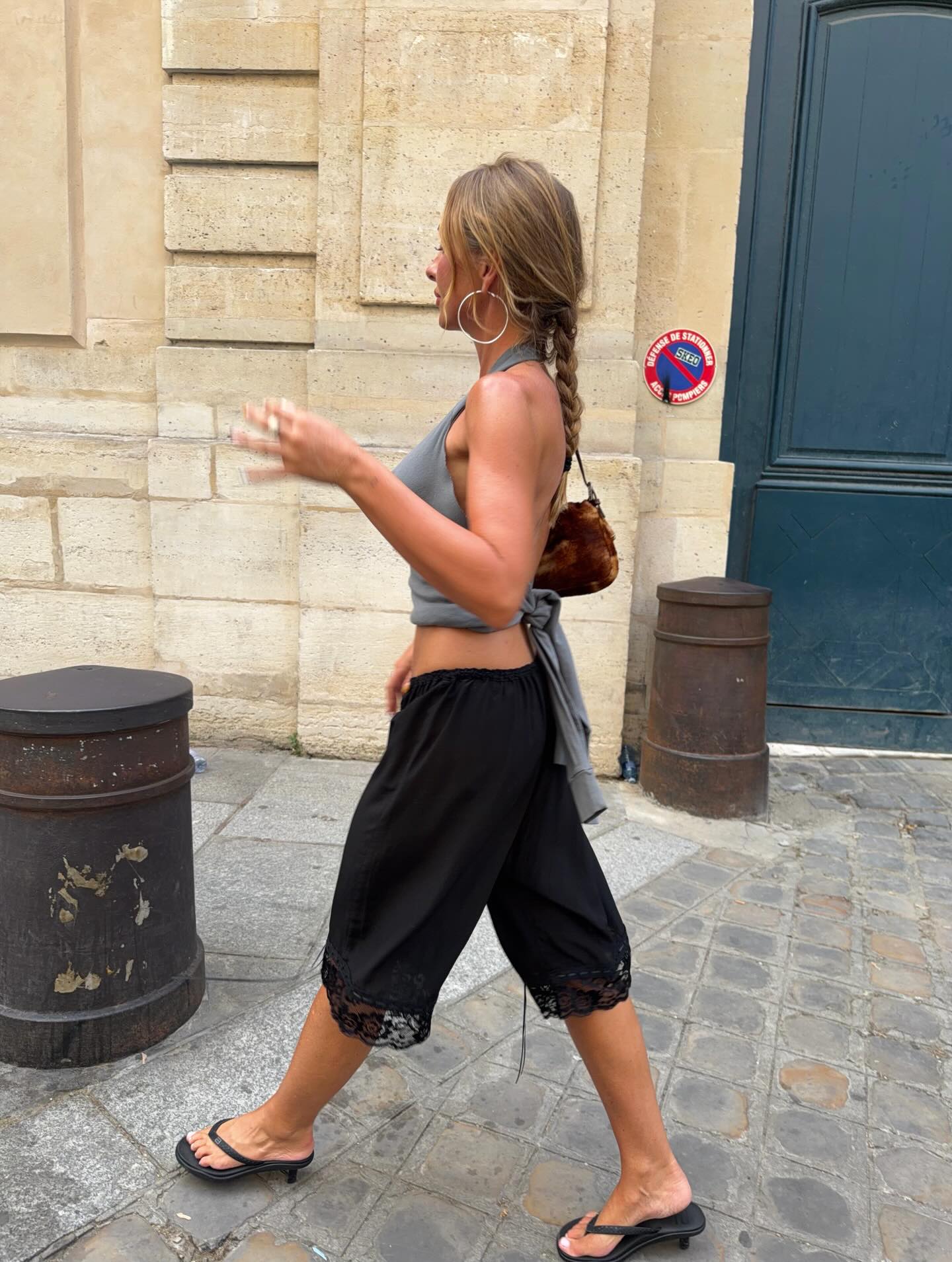 An image of @edenharper wearing a grey halterneck, black bloomer trousers and black kitten heel flip-flops, an example of a classic Mallorca summer outfit.