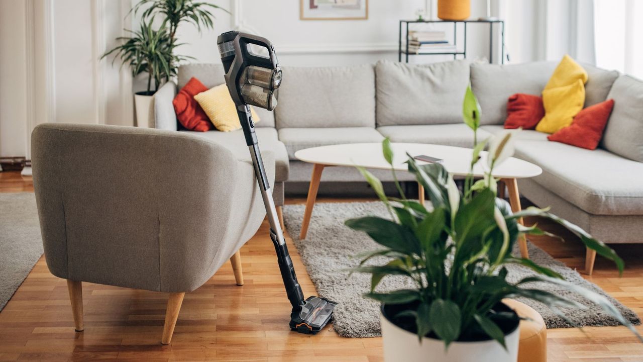 A cordless vacuum cleaner resting against an arm chair in a living room 