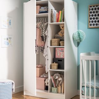 Tall white storage cupboard with doors open to see kids toys and clothes stored inside